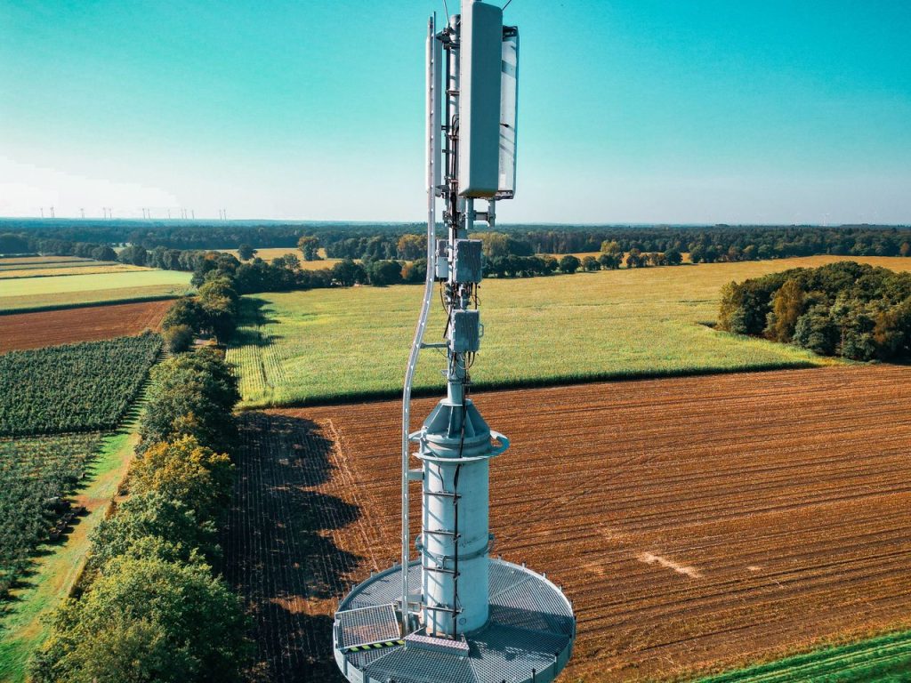 Sinal de internet pode reduzir barreiras à gestão e à inovação no campo Vista aérea de uma torre de telefonia cercada por áreas agrícolas.