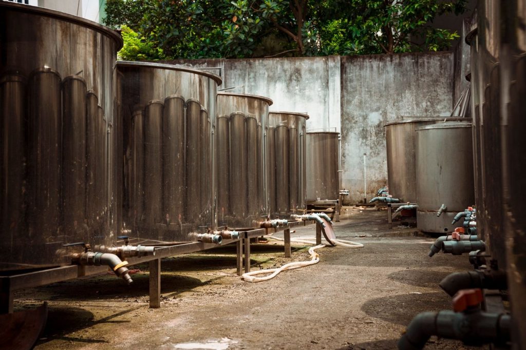 Grandes tanques metálicos industriais conectados por tubulações, em uma área externa de concreto.